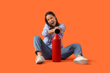 Young woman with fire extinguisher sitting on orange background