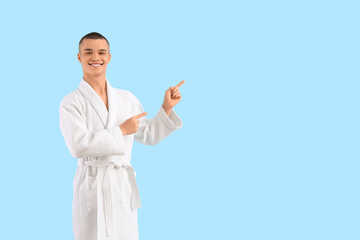 Teenage boy in bathrobe pointing at something on blue background