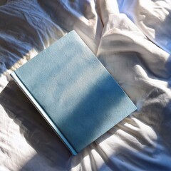 top view of light blue note book on cozy clean white bed sheet, sun shine, shadow