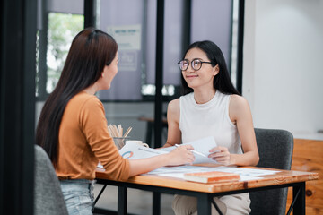 Fototapeta premium Two women having a professional discussion in a modern office setting, exchanging documents and ideas.
