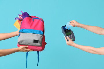 Female hands with backpack, school supplies, credit card and payment terminal on blue background,...