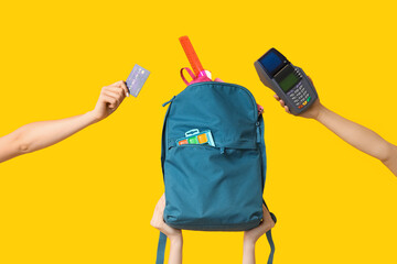 Female hands with backpack, school supplies, credit card and payment terminal on yellow background,...