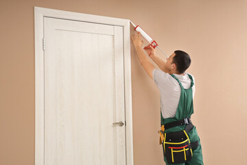 Male worker with caulking gun sealing cracks between door and wall at home