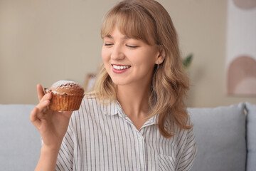 Young woman with tasty muffin at home, closeup