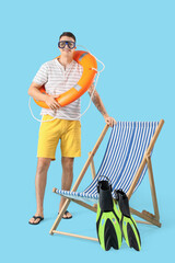 Young man with ring buoy and deck chair on blue background