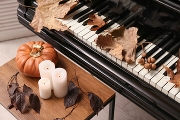 Ceramic pumpkin and burning candles on coffee table near piano keyboard with autumn leaves