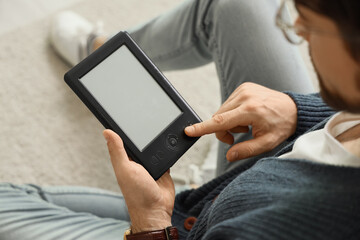 Young man with e-reader sitting on floor at home, closeup