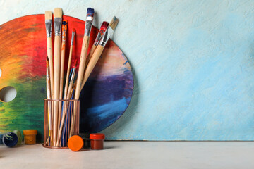 Artist brushes, paints and palette on white table against light blue background