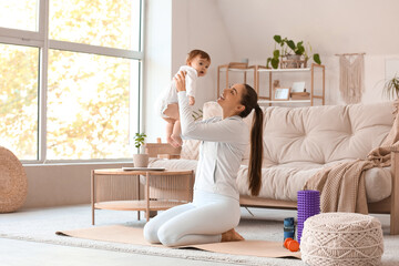 Sporty young mother with her little baby sitting on yoga mat at home