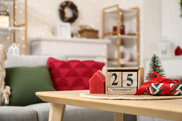 Obraz premium Cube calendar with date of Christmas, candle, toy fir tree and gift on table in living room, closeup