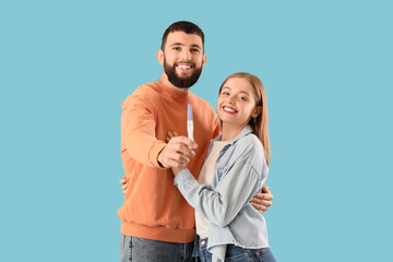Fototapeta premium Happy young couple with pregnancy test hugging on blue background