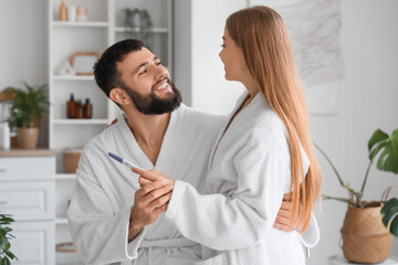 Happy young couple with pregnancy test hugging in bathroom