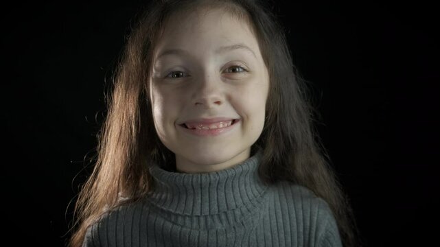 Child sign do not tells gossip secret. A view of joyful little girl close her mouth and show gesture on the black background.