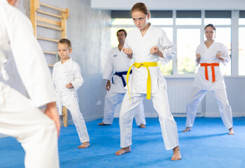 Teen girl and her family repeat movements and learn fighting techniques during martial arts lesson. Experienced man unrecognizable instructor conducts personal karate training for large family