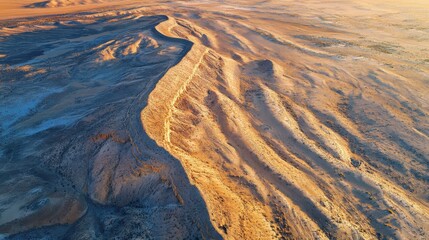 Fototapeta premium A stunning aerial view reveals a vast desert expanse, highlighted by soft golden hues. A winding river elegantly cuts through the arid landscape, showcasing nature's beauty at twilight.
