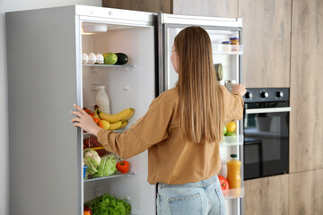 Young woman near open fridge in kitchen, back view