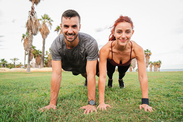 Energetic Couple Performs Synchronized Planks During Outdoor Workout Session in Palm Tree-Lined...