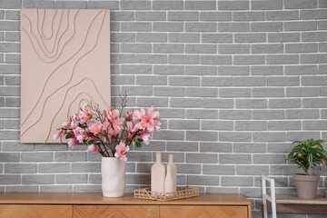 Vase with magnolia flowers on commode near grey brick wall in living room