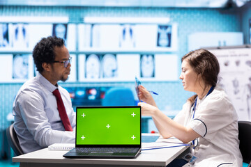 General practitioner and patient looking at green screen on device, recommending pills and drugs during check up visit. Diverse people discussing about diagnostics and remedy.