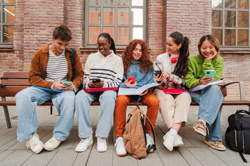 Diverse Group of College Students Engage with Their Smartphones While Studying Together on Campus Bench, Mixing Social Media and Academic Work Against Historic Brick Architecture