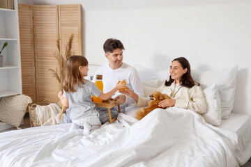 Little girl with her parents and Pomeranian dog having breakfast in bedroom