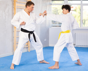 Fototapeta premium Adult man and teenage boy in kimono practicing karate fighting in gym