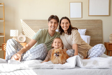 Happy little girl with her parents and Pomeranian dog sitting in bedroom