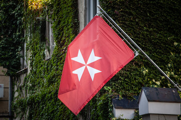 The flag of the Sovereign Military Order of Malta waves prominently with its distinctive red flag &...