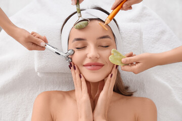 Young woman and hands with facial massage tools on couch in beauty salon, top view