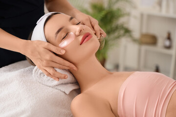 Young woman with under-eye patches getting facial massage in beauty salon, closeup