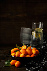Fresh kumquat fruits in pan, glasses and towel on wooden background