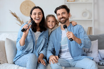 Happy parents with microphones and their little daughter singing karaoke on sofa at home