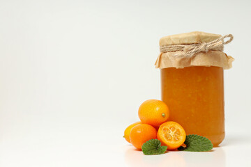 Fresh kumquat fruits and glass jar with jam on white background, space for text