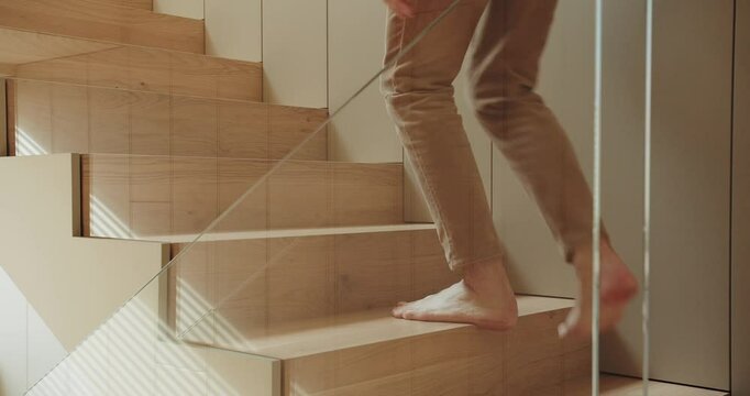 A person walks barefoot up a wooden staircase in a modern, minimalist home, featuring natural light and sleek design. Barefoot Person Ascending Modern Wooden Staircase in Minimalist Home