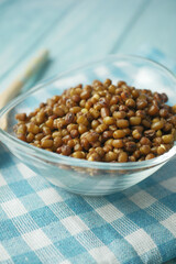 A beautiful glass bowl filled with brown sprouted mung beans sitting on a blue checkered tablecloth