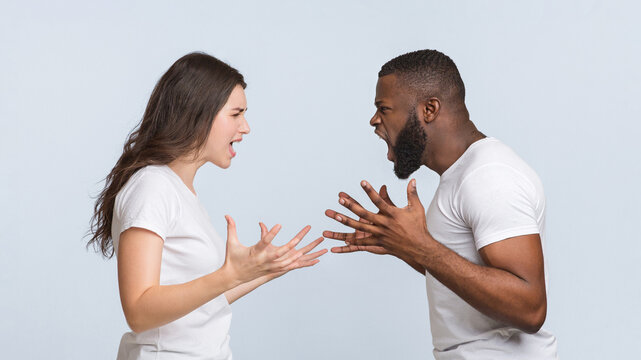 Relationship crisis. Furious multiracial couple yelling at each other, emotionally arguing and gesturing over light studio background, panorama