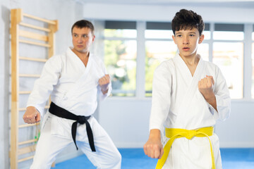 Fototapeta premium Active middle-aged and teenage male attendees of karate classes practicing kata in sports hall