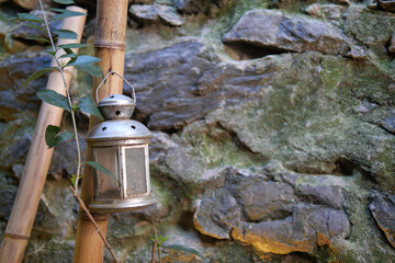 A rustic lantern is beautifully hanging on a weathered stone wall, surrounded by bamboo