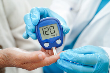 Asian doctor using digital glucose meter for check sample blood sugar level to treatment diabetes.