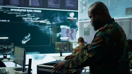 Army espionage specialist in a control center collecting satellite cctv data real time surveillance, strategic military operations. Working to ensure national security and protocols. Camera B.