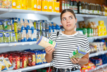 Young girl stands in cereal section of supermarket and chooses pack of peas