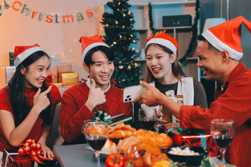 Group of young Asian man and women as friends having fun at a New Year's celebration, holding gift boxes standing by Christmas tree decoration, midnight countdown Party at home with holiday season.