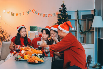 Group of young Asian man and women as friends having fun at a New Year's celebration, holding gift boxes standing by Christmas tree decoration, midnight countdown Party at home with holiday season.