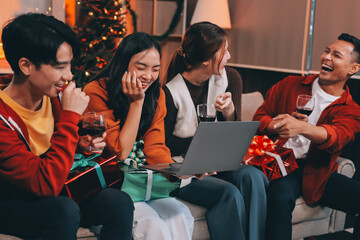 Group of young Asian man and women as friends having fun at a New Year's celebration, holding gift boxes standing by Christmas tree decoration, midnight countdown Party at home with holiday season.