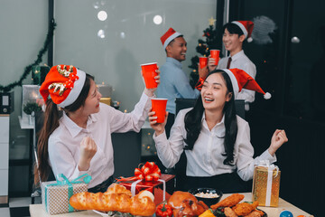 full length view of a group of business team wearing red Santa hat and exchange gift box together in the office for Christmas.