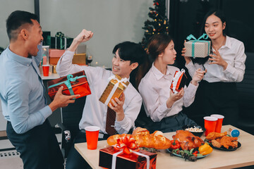 full length view of a group of business team wearing red Santa hat and exchange gift box together in the office for Christmas.