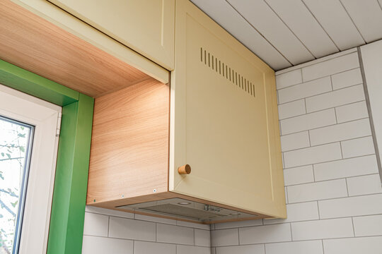 Fragment of upper kitchen cabinets with yellow facades and wooden knobs installed on tiled wall around window