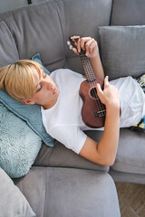 Young person playing ukulele while lounging on a couch.