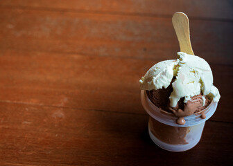 A cup of vanilla and chocolate ice cream with scoop on wooden table