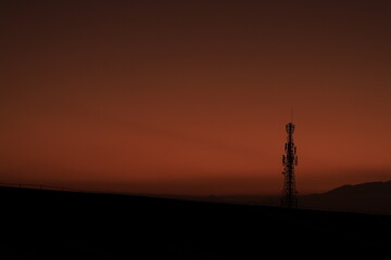 Obraz premium Silhouette of Communication Tower at Sunset with Orange Sky